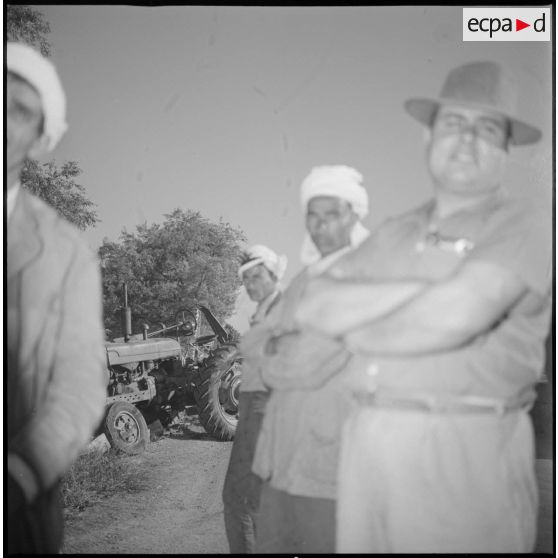 Portrait d'un groupe de personnes. Au second plan, un tracteur. Le premier plan de la photographie est flou. [légende d'origine]