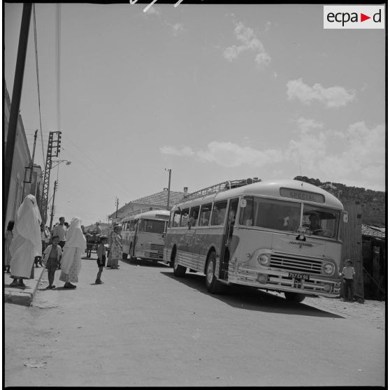 En ville, deux bus venus récupérer des enfants stationnent en attendant le départ pour les emmener au Camp des chasseurs du 8e RIM. [légende d'origine]