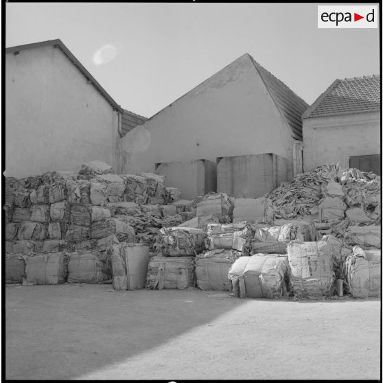 [Papeterie d'Aïn-el-Hadjar. Vue sur des matériaux conditionnés et stockés à l'extérieur, devant des bâtisses.]