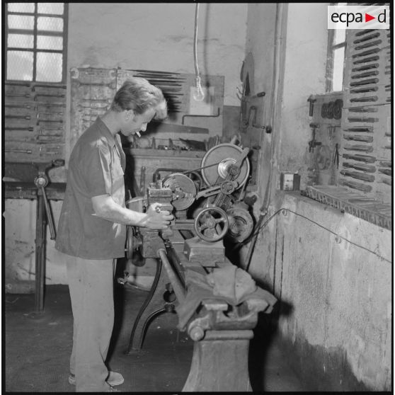 [Papeterie d'Aïn-el-Hadjar. Un ouvrier, entouré d'outils, travaille à l'aide d'une machine dans un atelier.]