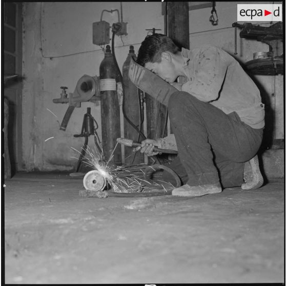 [Papeterie d'Aïn-el-Hadjar. Un ouvrier, accroupi au sol, effectue un travail de soudure.]