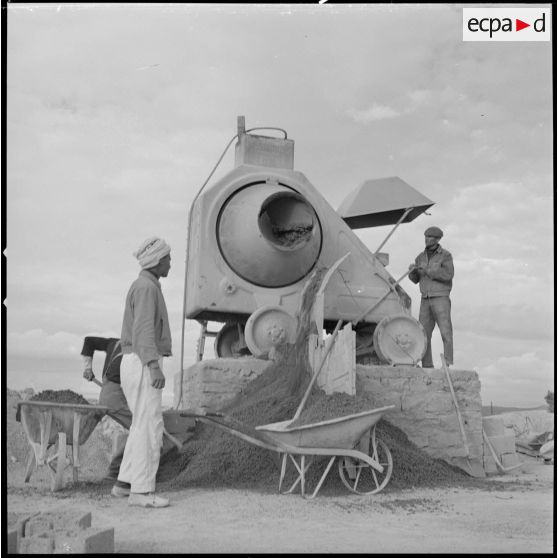 [Trois ouvriers travaillent avec un engin utilisé pour la construction des nouvelles bâtisses du centre de regroupement de la ferme Cazorla. ]
