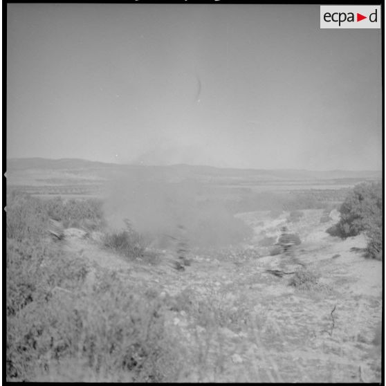 [Entraînement de parachutistes dans le Vieux Saïda. Soldats courant sur un terrain enfumé par des munitions d'exercices.]