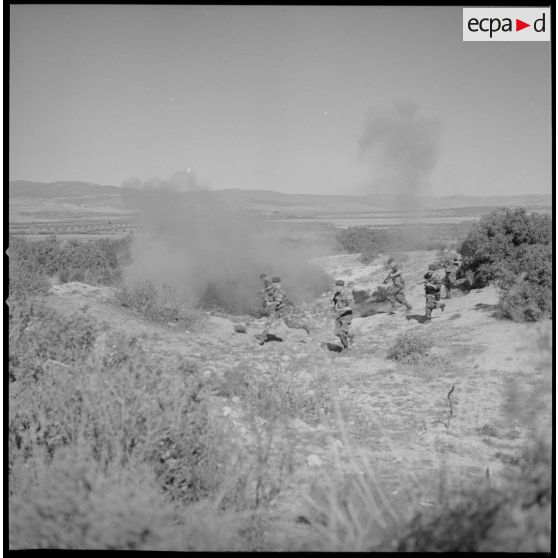 [Entraînement de parachutistes dans le Vieux Saïda. Soldats courant sur un terrain enfumé par des munitions d'exercices.]