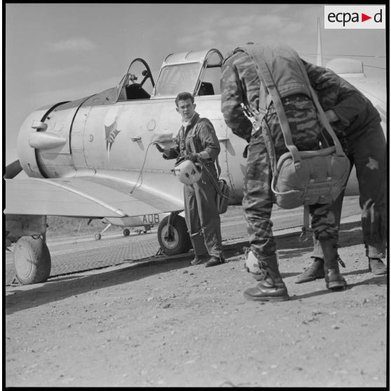 [Aérodrome de Nazereg-Flinois. Le photographe Arthur Smet, de dos, s'équipe d'un parachute pour un vol de reconnaissance à bord d'un avion North American T-6 piloté par un lieutenant, de face, de l'escadrille d'aviation légère d'appui (EALA).]