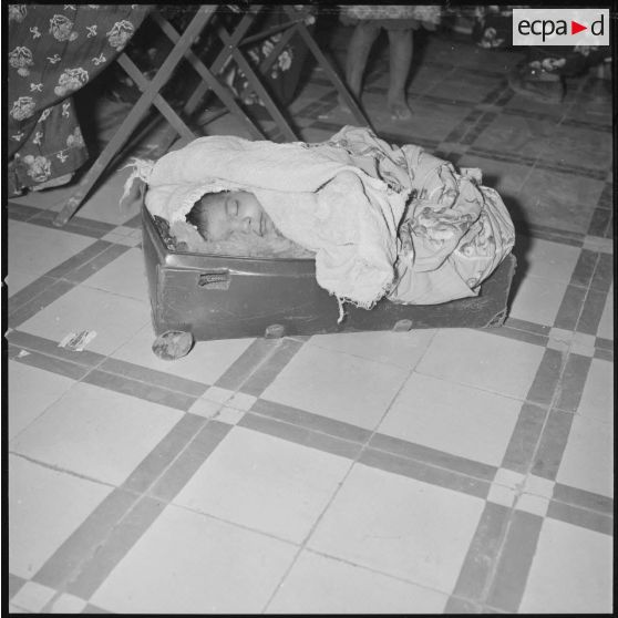 [Nourrisson dormant dans une valise lors d'un atelier de couture à Aïn el Hadjar.]