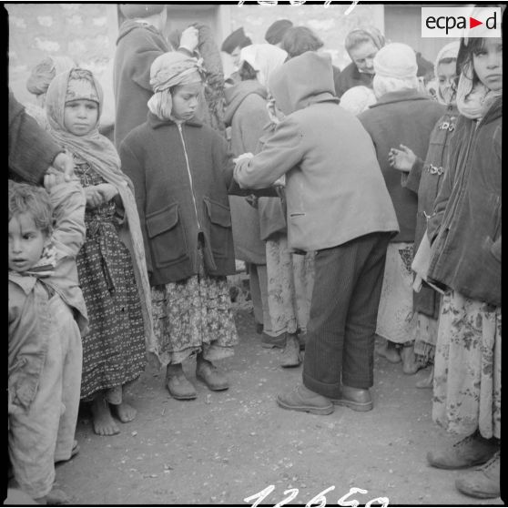 [Poste de Tamesna, région de Saïda. Enfant, venue de France, aidant une autre enfant à mettre un manteau donné à l'occasion d'une action caritative initiée par des Luxembourgeois.]
