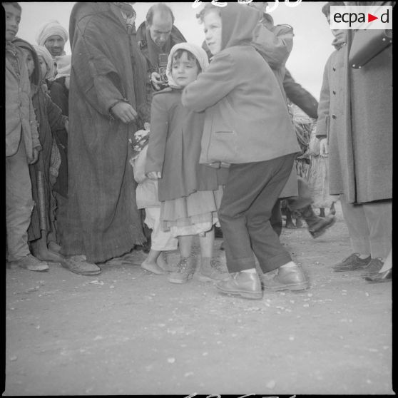 [Poste de Tamesna, région de Saïda. Enfant, venue de France, aidant une autre enfant à mettre un manteau donné à l'occasion d'une action caritative initiée par des Luxembourgeois.]