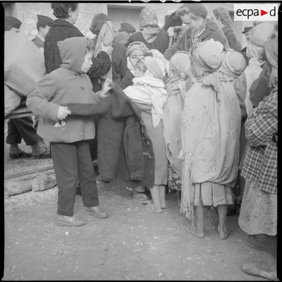 [Poste de Tamesna, région de Saïda. Enfant, venue de France, aidant une autre enfant à mettre un manteau donné à l'occasion d'une action caritative initiée par des Luxembourgeois.]