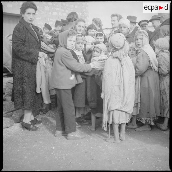 [Poste de Tamesna, région de Saïda. Enfant, venue de France, aidant une autre enfant à mettre un manteau donné à l'occasion d'une action caritative initiée par des Luxembourgeois.]