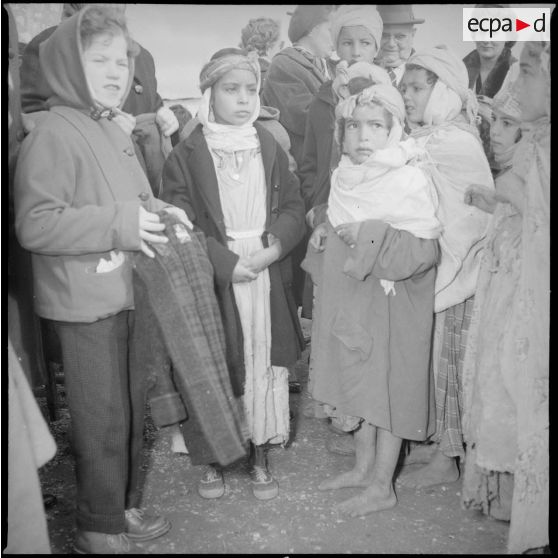 [Poste de Tamesna, région de Saïda. Enfant, venue de France, distribuant des manteaux donnés à l'occasion d'une action caritative initiée par des Luxembourgeois.]