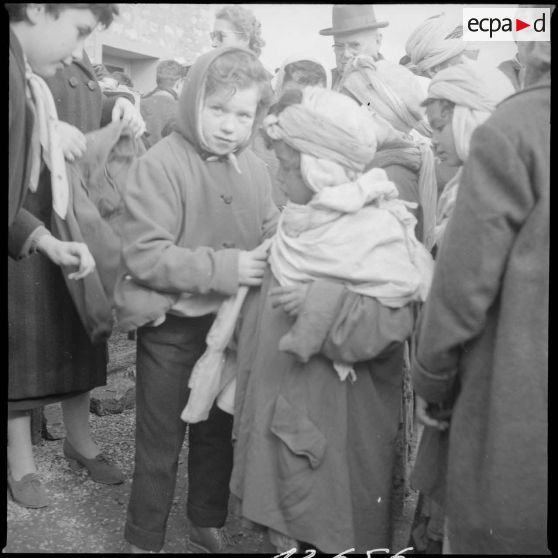 [Poste de Tamesna, région de Saïda. Enfant, venue de France, aidant une autre enfant à mettre un manteau donné à l'occasion d'une action caritative initiée par des Luxembourgeois.]
