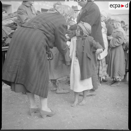 [Poste de Tamesna, région de Saïda. Femme aidant une enfant à mettre un manteau donné à l'occasion d'une action caritative initiée par des Luxembourgeois.]