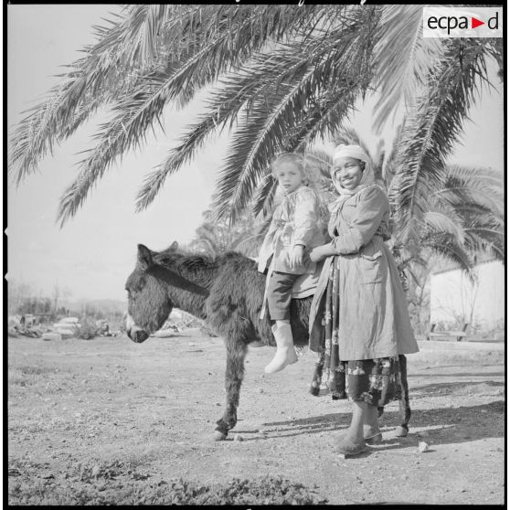 [Enfant posant à dos d'âne avec une jeune fille d'origine algérienne dans une ferme près de Nazareg.]