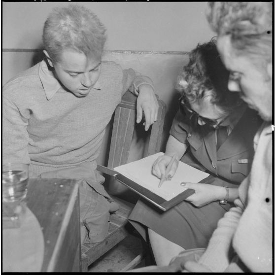 Une femme de la Croix-Rouge prend des notes auprès d'hommes du CEFEO (Corps expéditionnaire français en Extrême-Orient) récemment libérés.
