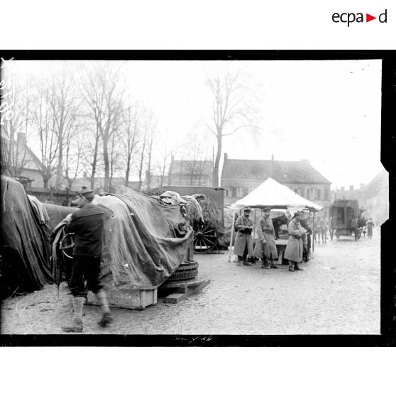 Des pièces de marine recouvertes d'une bâche sur la place de Rexpoëde. [légende d'origine]