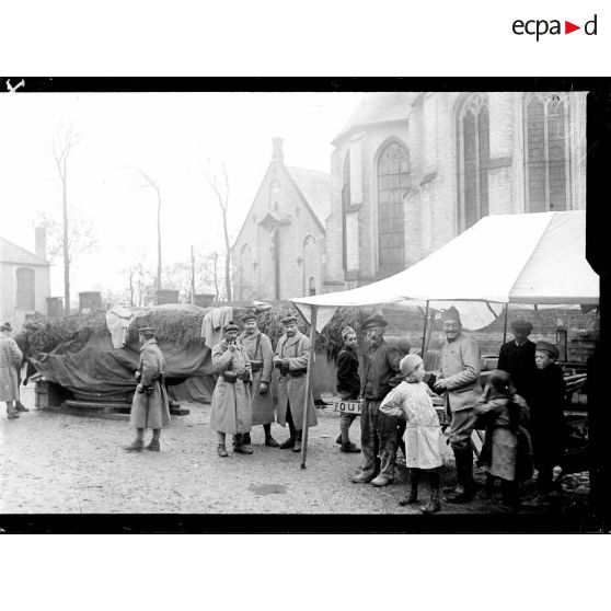 Des pièces de marine recouvertes d'une bâche sur la place de l'église de Rexpoëde. [légende d'origine]