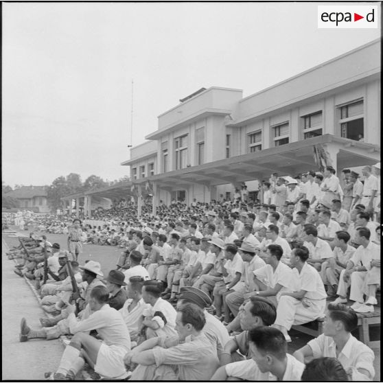 Dans les gradins du stade Mangin, les spectateurs regardent le match de football opposant l'équipe de Nam-Hoa à la sélection Nord-Vietnam.