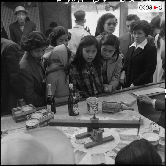 Jeunes filles devant un stand de la kermesse organisée au profit des invalides et des blessés de guerre d'Hanoï.
