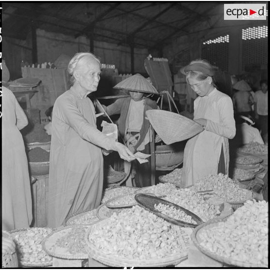 Une femme tend un billet au-dessus d'un étal de marchandise au grand marché d'Hanoï.
