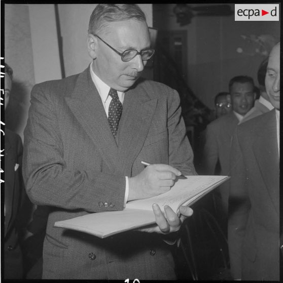 M. Pleven, ministre de la Défense nationale, signe le livre d'or du camp de presse d'Hanoï.