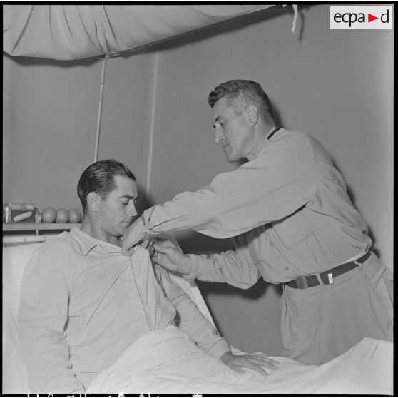 L'adjudant-chef Bartier, pilote d'hélicoptère blessé à Diên Biên Phu, réçoit des mains du général Dechaux, les insignes d'officier de la Légion d'honneur et la croix de guerre des TOE avec palme.
