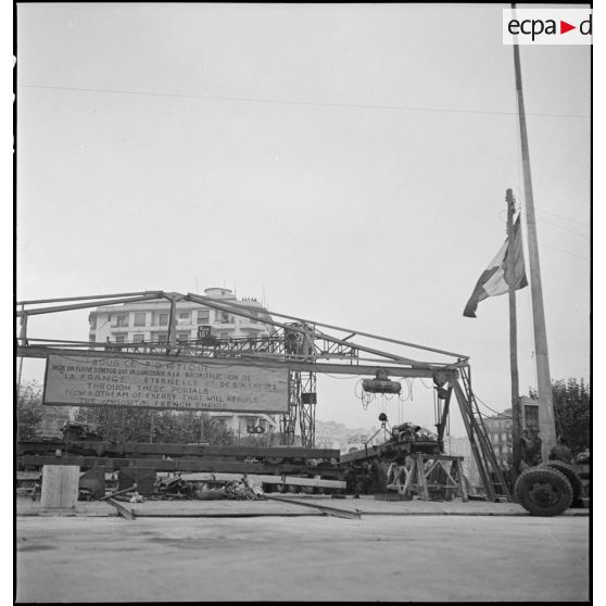 Le portique surmontant une chaîne de montage de matériels américains installée sur le port d'Alger. La pancarte accrochée au portique porte l'inscription galvanisante : " Sous ce portique passe un fleuve d'énergie qui va concourir à la reconstruction de la France éternelle et de son empire ".