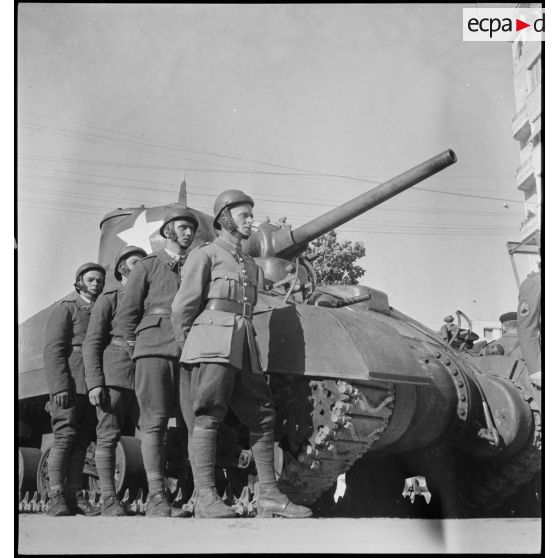 Lors d'une cérémonie franco-américaine de remise de matériel américain aux troupes françaises, l'équipage d'un char Sherman M4 du 5e RCA (régiment de chasseurs d'Afrique) de la 1re DB (division blindée) se tient près du blindé qu'il a perçu.