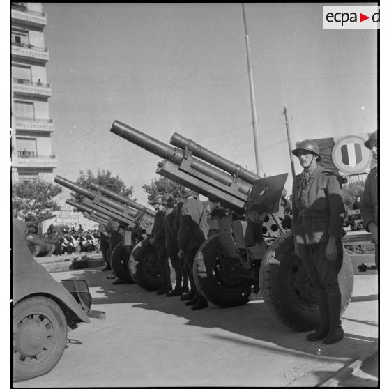 Sur le champ de manoeuvres d'Alger, lors d'une cérémonie franco-américaine de remise de matériels américains aux troupes françaises, des artilleurs des 1er et 2e groupes du 63e RAA (régiment d'artillerie d'Afrique) de la 2e DIM (division d'infanterie marocaine) sont sur les rangs avec leurs nouvelles dotations d'obusiers de 105 mm Howitzer M2.