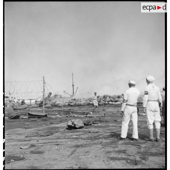 Des marins américains de la MP (police militaire ou military police) regardent un navire pétrolier incendié dans le port d'Alger.