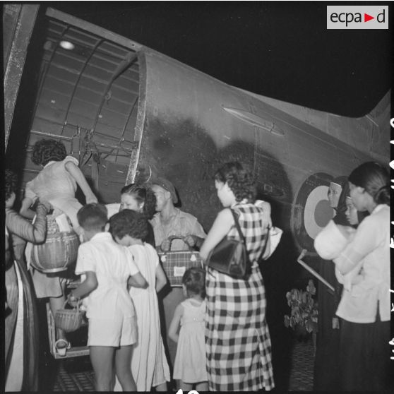 Sur la base aérienne, des réfugiés montent à bord d'un avion Dakota du pont aérien.