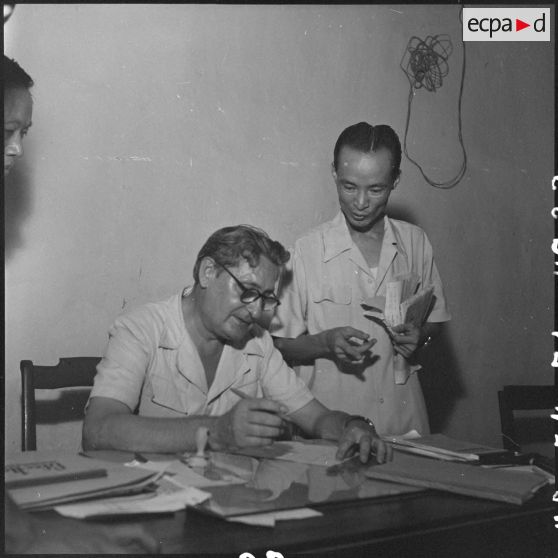 Assis à son bureau le directeur du centre des réfugiés d'Hanoï prépare ses listes.