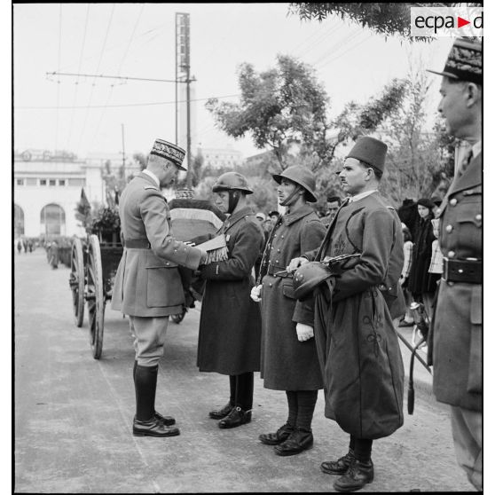 Le général d'armée Henri Giraud, commandant en chef civil et militaire, lors de la cérémonie d'obsèques du général de division Marie-Joseph Welvert, remet les insignes de grand-croix de la Légion d'honneur au défunt qu'il accroche sur le coussin de ses décorations.