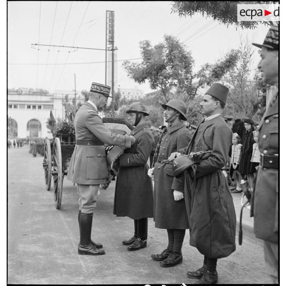Le général d'armée Henri Giraud, commandant en chef civil et militaire, lors de la cérémonie d'obsèques du général de division Marie-Joseph Welvert, remet les insignes de grand-croix de la Légion d'honneur au défunt qu'il accroche sur le coussin de ses décorations.