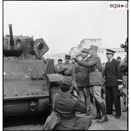Sur une chaîne de montage sur le port d' Alger, le général de division Roger Leyer, aide-major général chargé de l'organisation, donne des informations concernant un char léger Stuart M5A1 au général d'armée Henri Giraud, commandant en chef civil et militaire, dans le cadre du réarmement de l'armée française par les Etats-Unis. Au premier plan, un caméraman du United States army signal corps.