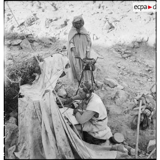 Deux méharistes du groupement Paganelli utilisent un central téléphonique dans le secteur du Chott el Jerid, sur le FSEA (Front sud-est algérien). Le méhariste au second plan actionne la génératrice à manivelle.