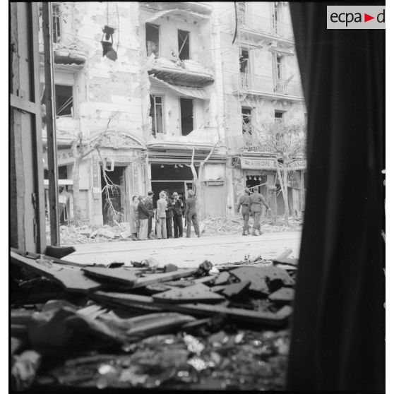 Des civils discutent devant un immeuble endommagé de la rue d'Isly après le bombardement allemand visant l'aérodrome Maison-Blanche à Alger, dans la nuit du 20 au 21 novembre 1942.