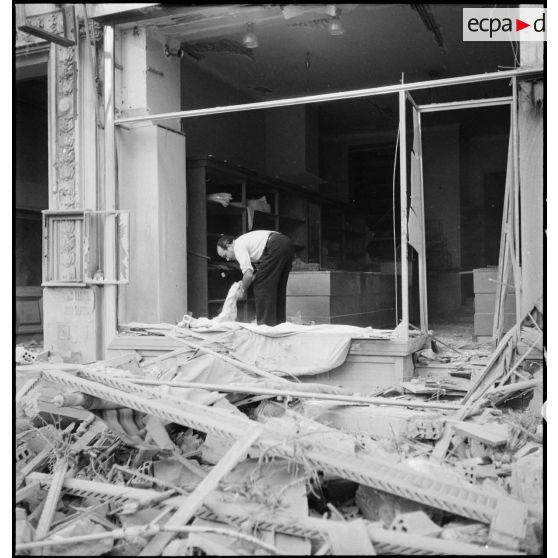 Un commerçant déblaie la vitrine de sa boutique endommagée de la rue d'Isly après le bombardement allemand visant l'aérodrome Maison-Blanche à Alger, dans la nuit du 20 au 21 novembre 1942.