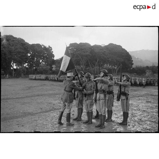 Le lieutenant-colonel Guillebaud, commandant l'école d'élèves aspirants, remet le drapeau de l'école au porte-drapeau de la garde lors du baptême de la promotion Tunisie.