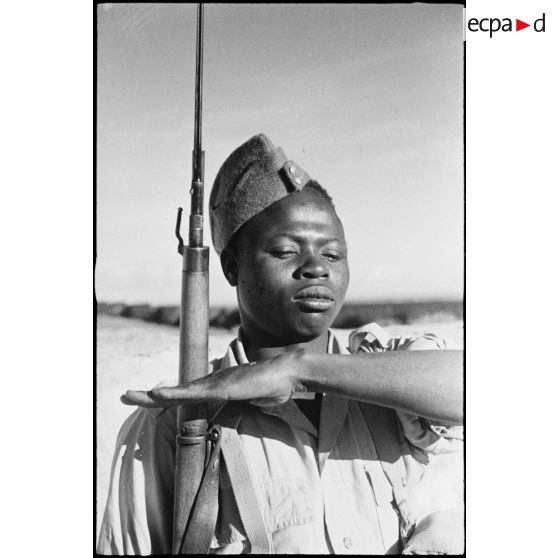 Portrait d'un tirailleur sénégalais, équipé à la britannique, au présentez-armes lors d'une inspection.