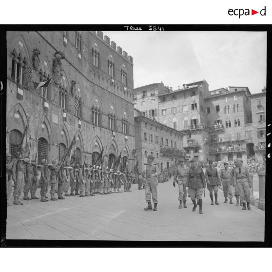 Lors d'une cérémonie, le général d'armée Alphonse Juin, commandant le corps expéditonnaire français (CEF), accompagnés de ses grands subordonnés, salue les drapeaux des unités alignés sur la Piazza del Campo à Sienne.