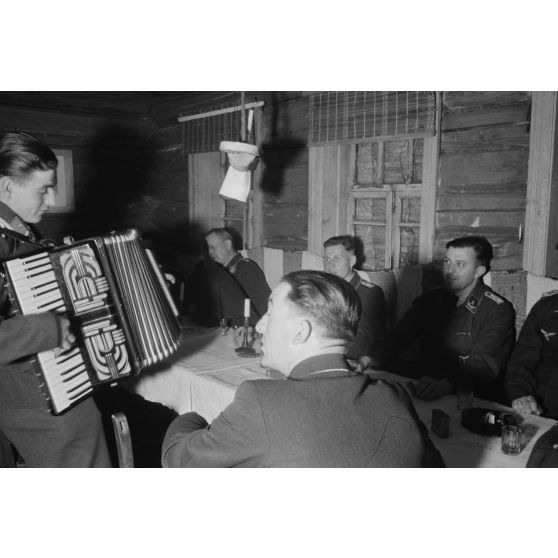 Des officiers de la Luftwaffe lors d'un repas, un sous-officier joue de l’accordéon.