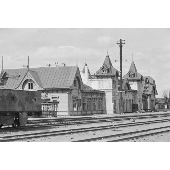 Une gare ferrovaire de taille moyenne, au premier plan un wagon blindé portant un camouflage.