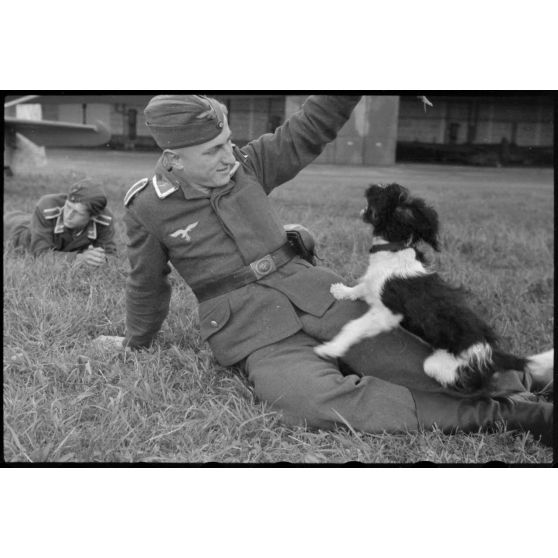 En Norvège, sur l'aérodrome de Stavanger-Sola, lors d'une démonstration 8./LLG 1 (Lulftlandegeschwader 1), un sous-officier joue avec un chien, mascotte de l'unité.