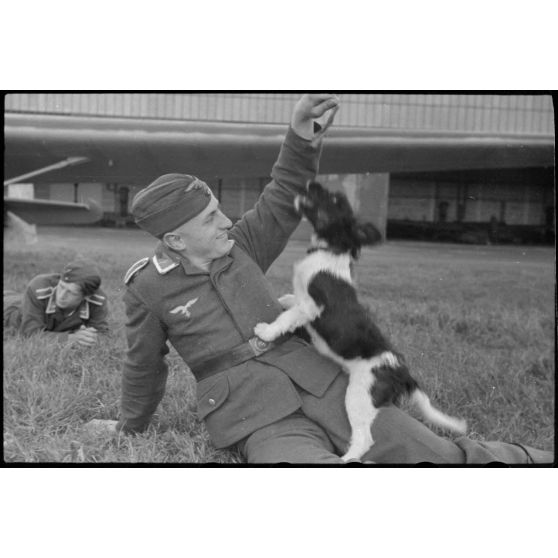 En Norvège, sur l'aérodrome de Stavanger-Sola, lors d'une démonstration 8./LLG 1 (Lulftlandegeschwader 1), un sous-officier joue avec un chien, mascotte de l'unité.