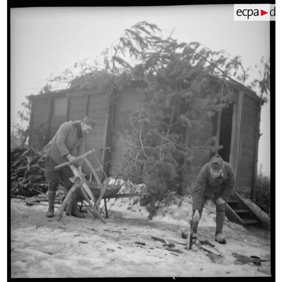 Deux soldats coupent du bois dehors près d'une baraque en bois.