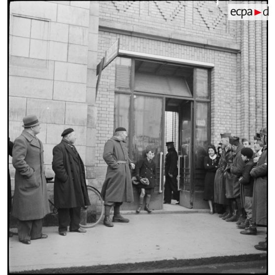 Civils et militaires attendent l'arrivée de comédiens, dont Fernandel à la sortie d'une gare.