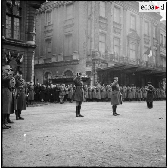 Plan général d'une cérémonie militaire, au premier plan divers officiers, dont un général de brigade, saluent.
