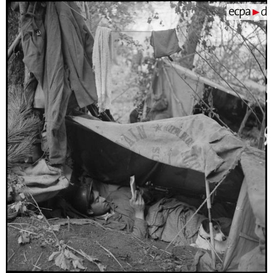Plan moyen d'un soldat qui lit allongé dans son trou de combat individuel.