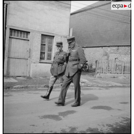 Deux officiers marchent dans une rue de village.